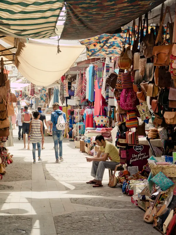 A shaded souk lane lined with leather bags, lamps and textiles